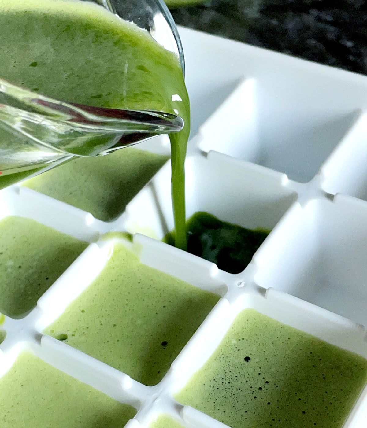 Green liquid being poured into a white ice cube tray.