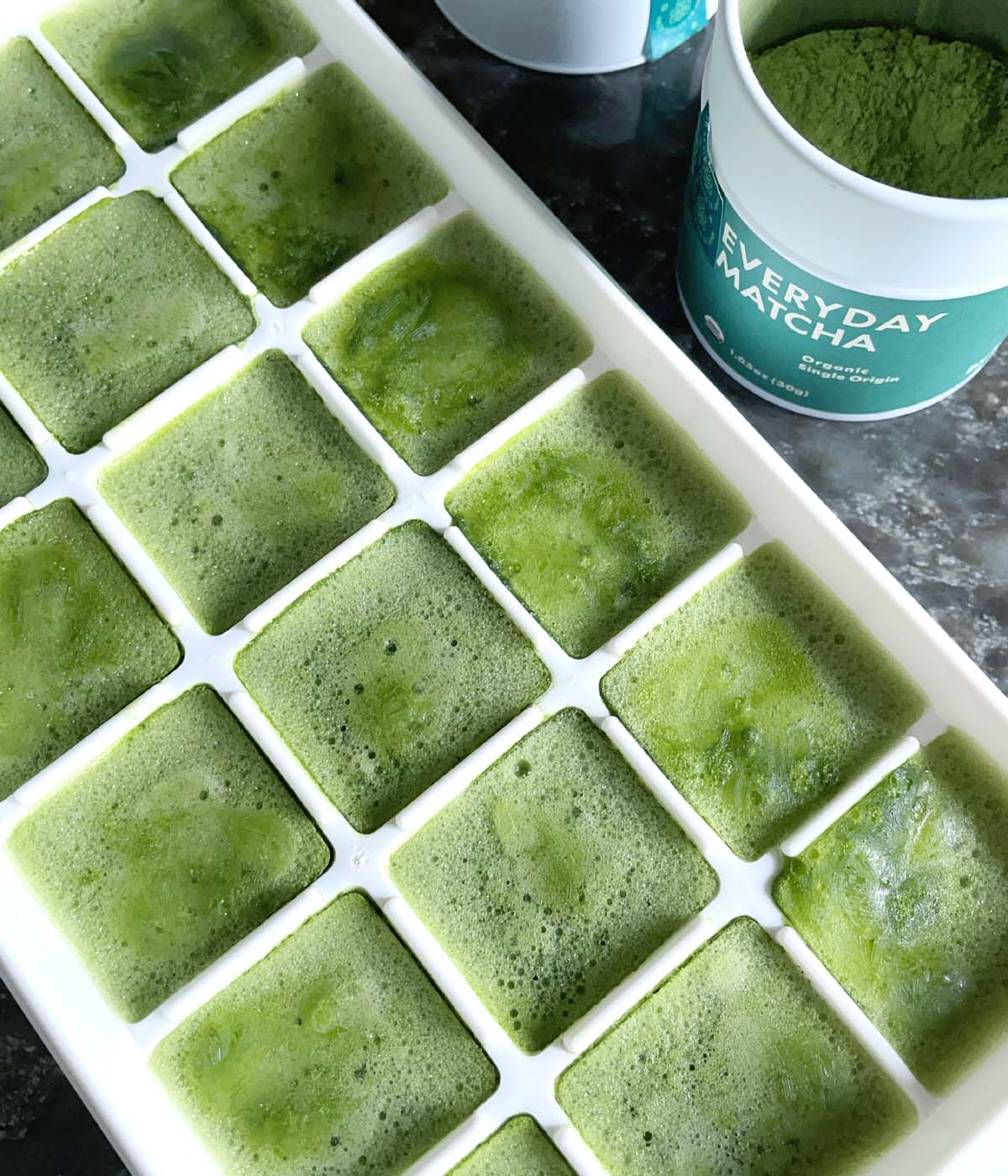 A white ice cube tray with green square ice cubes.