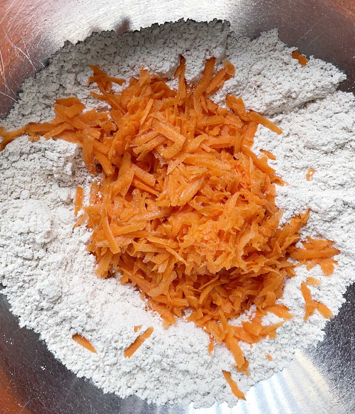 Grated orange carrot in a bowl containing white flours.