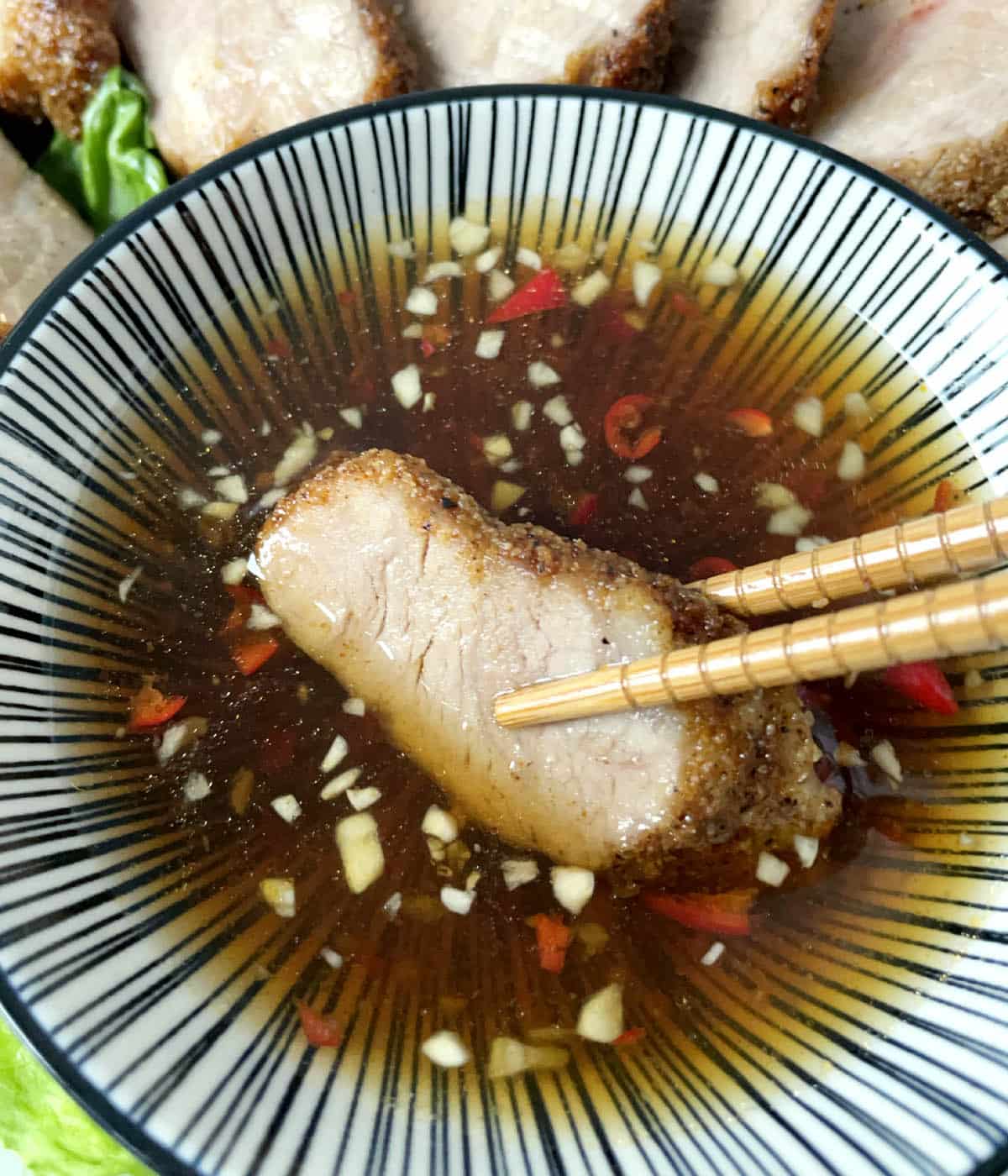 Wooden chopsticks dipping a spice of meat in a round bowl of dipping sauce.