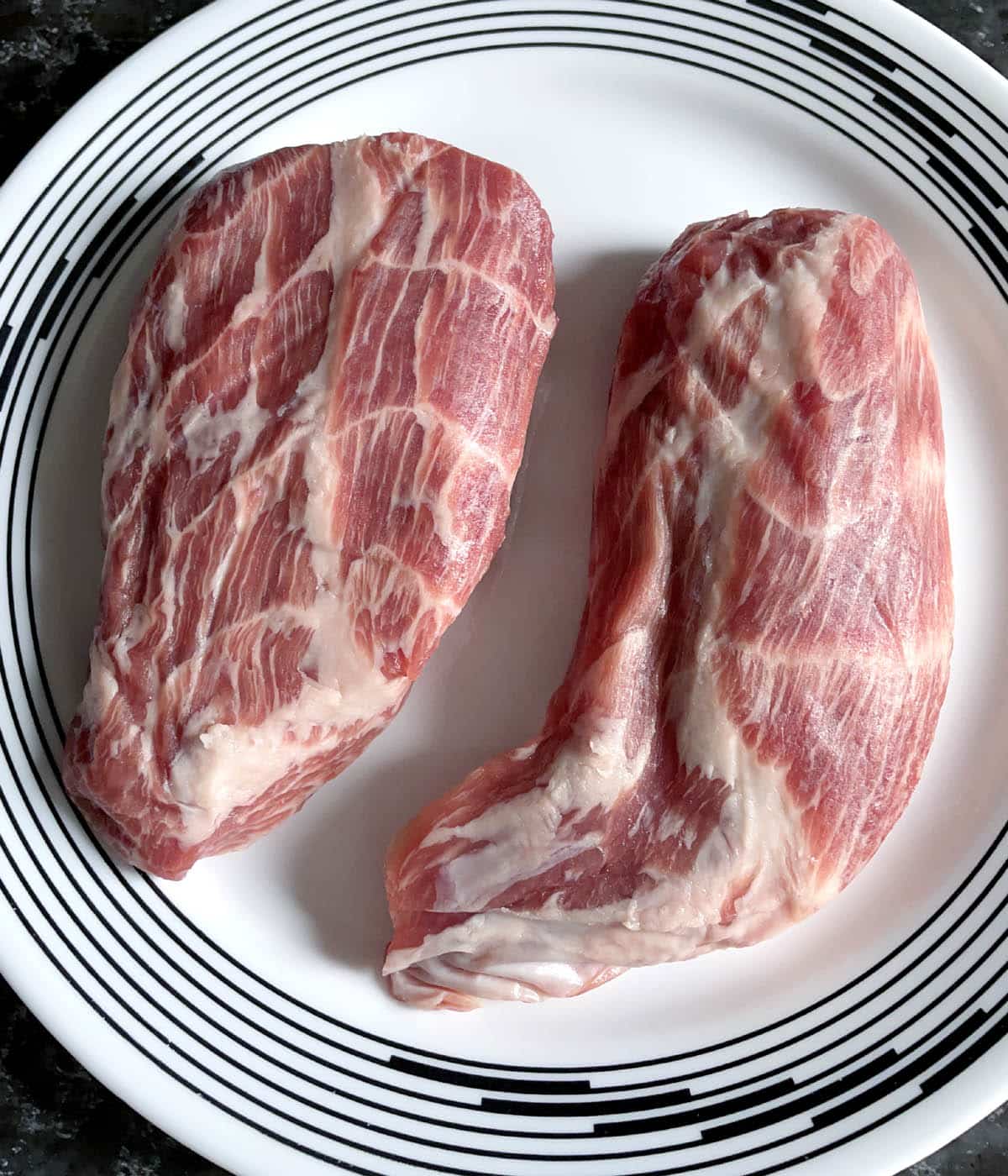 Two raw pieces of pork on a round white plate.