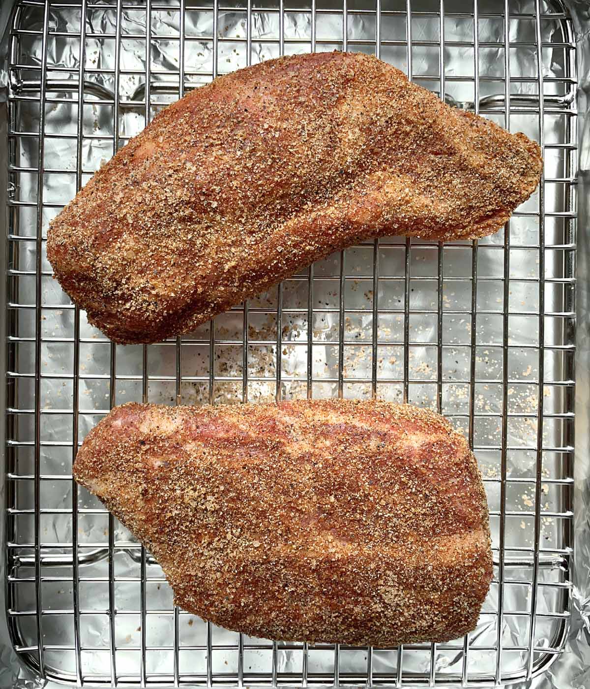 Two spice-coated pieces of meat on a metal rack in a baking pan.