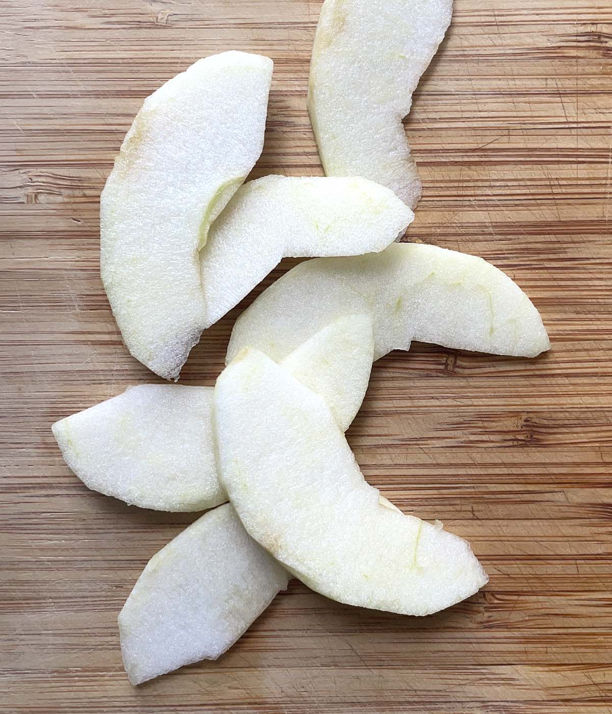 Slices of peeled apple on a wooden cutting board.