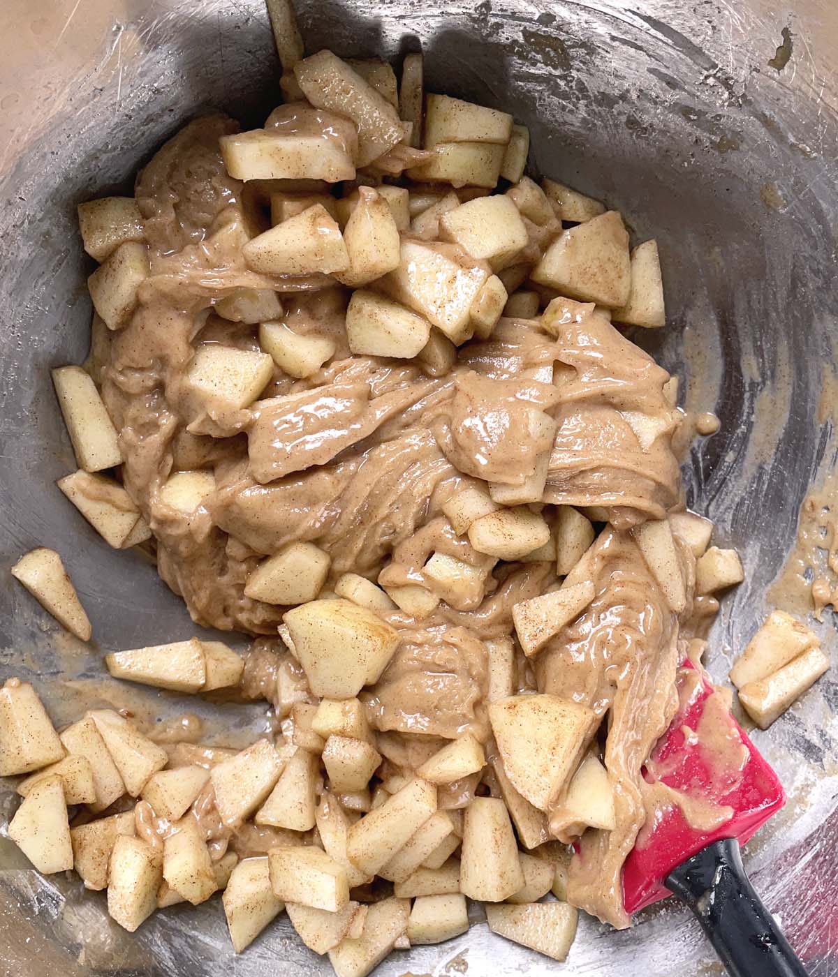 Diced apples being mixed into a light brown batter in a bowl.