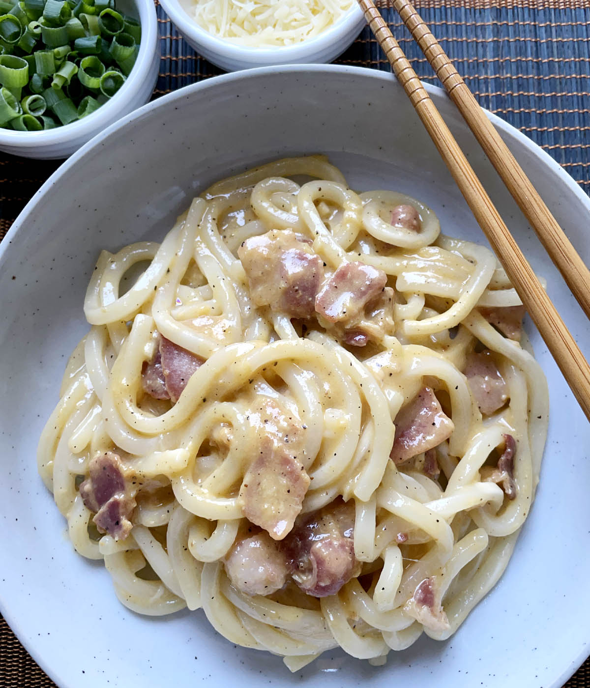 A round bowl containing saucy thick noodles and cooked bacon.