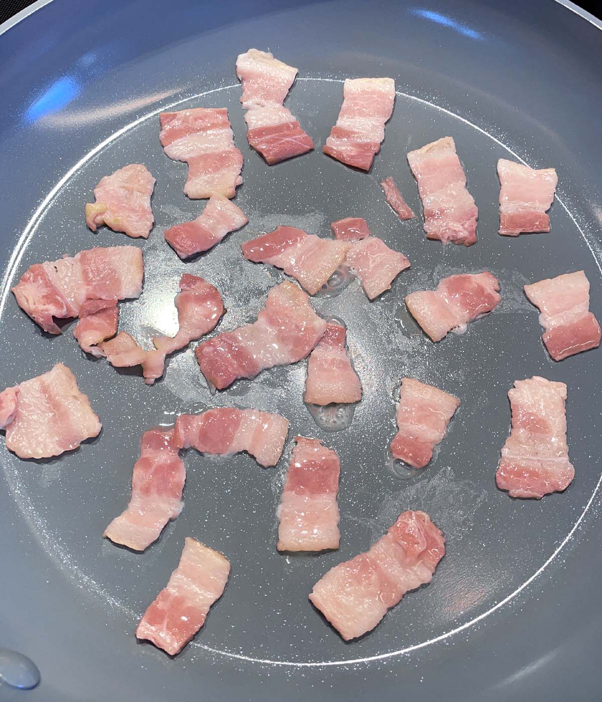 Pieces of raw bacon in a grey skillet.