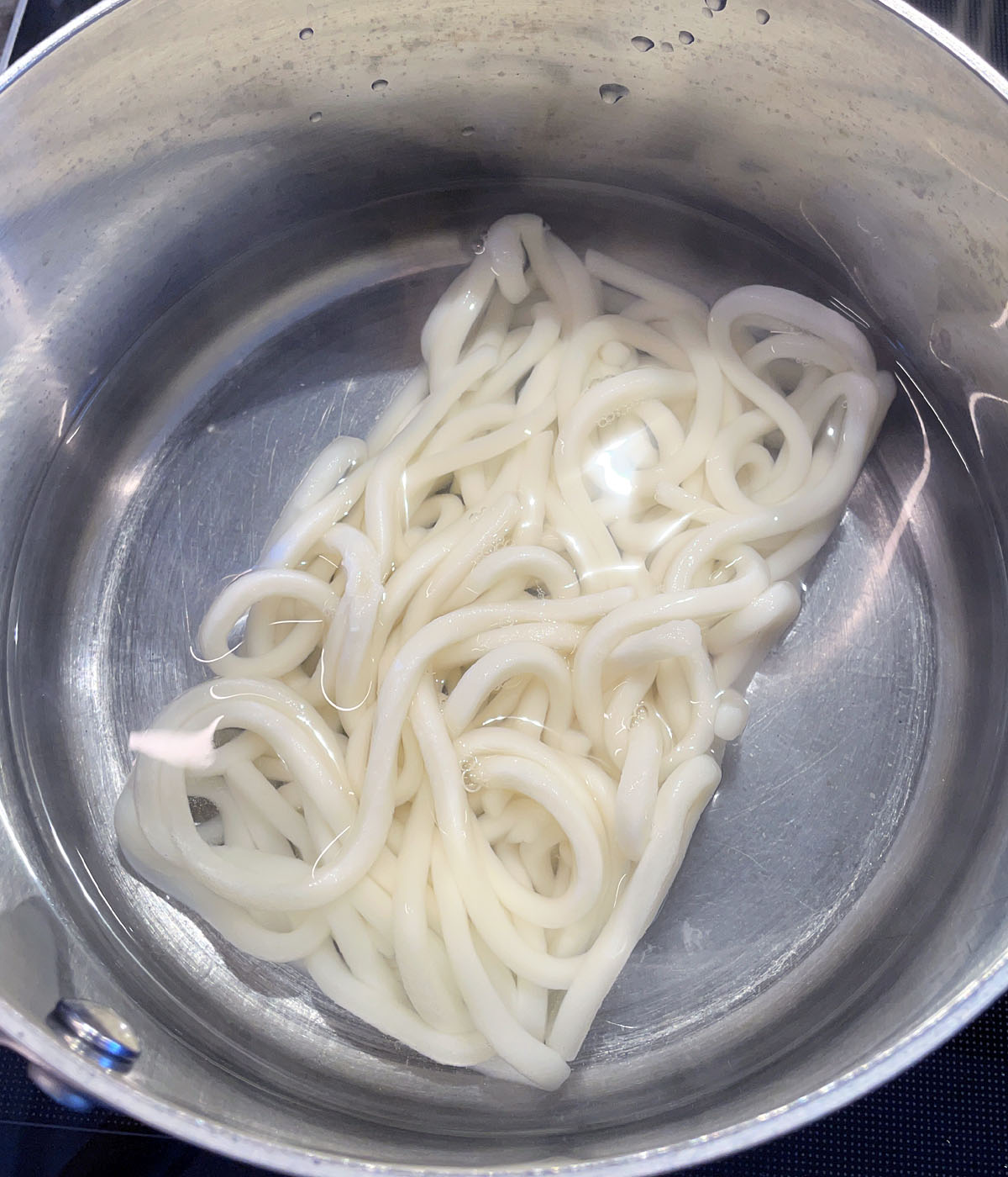 A metal pot containing a white brick of noodles in water.