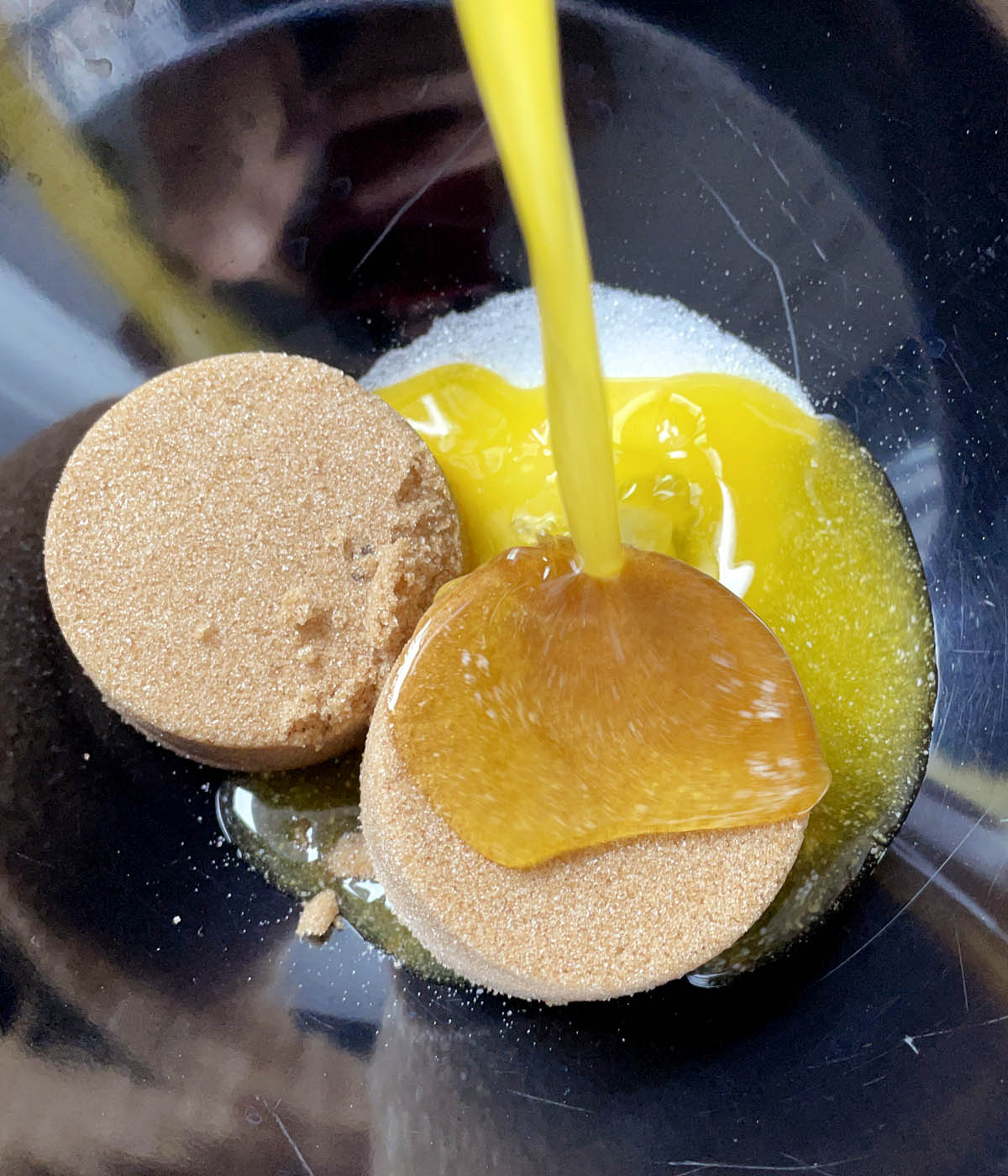 Melted butter being poured into a bowl containing white and brown sugars.