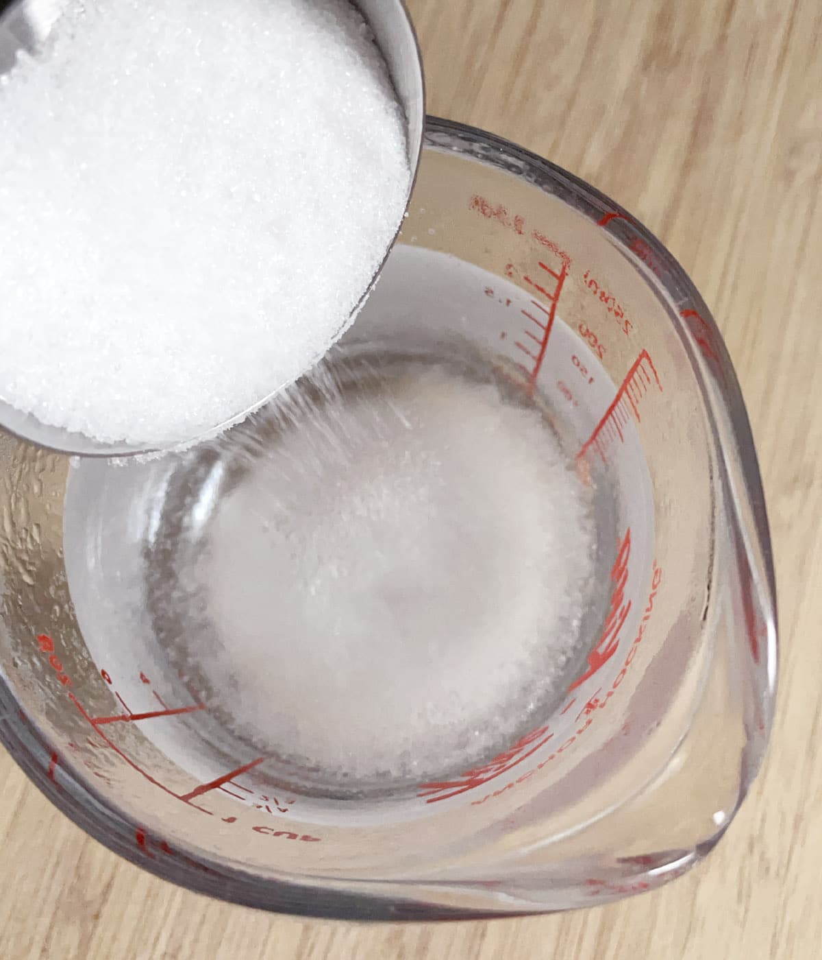 White sugar being poured into a measuring cup containing water.
