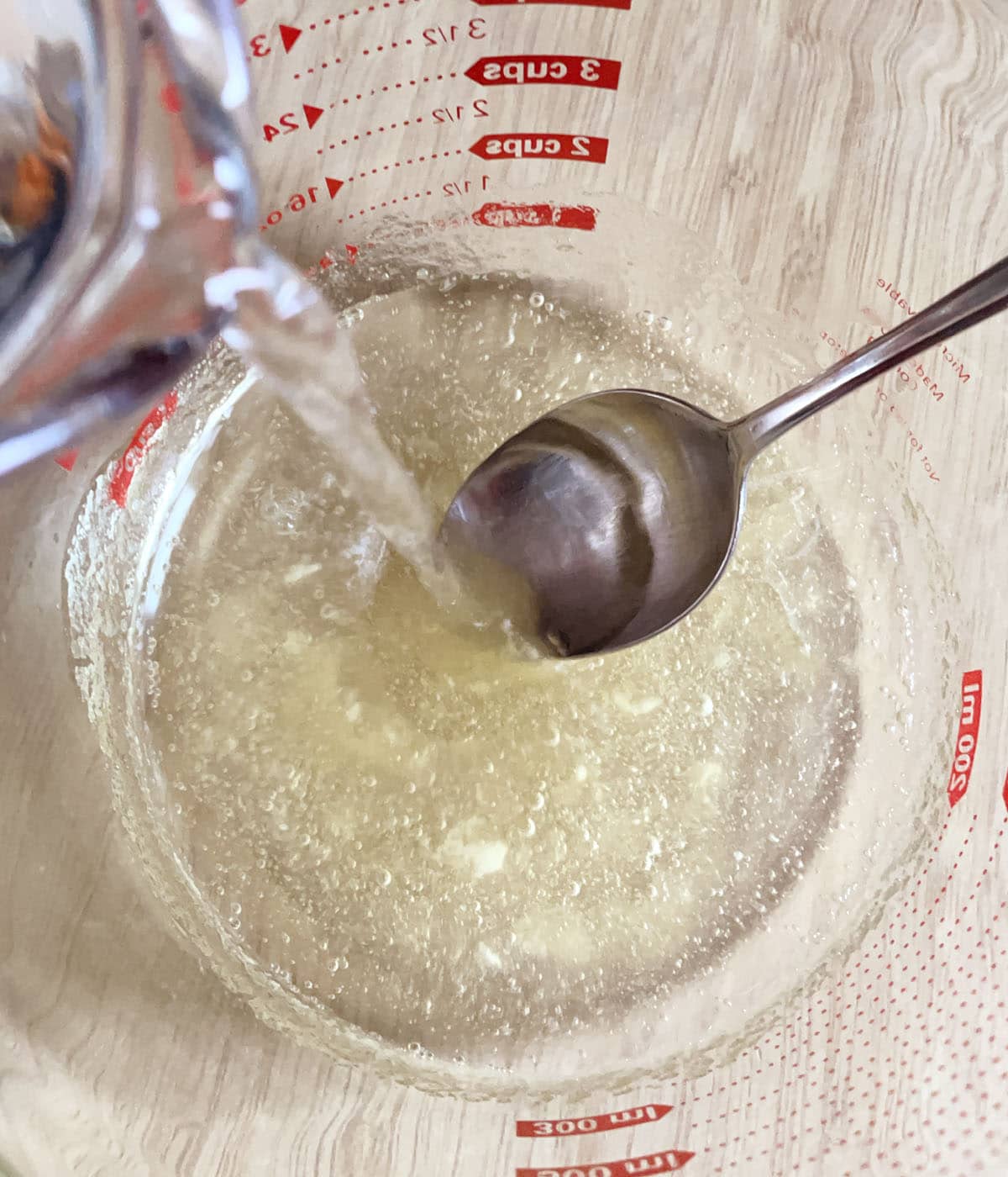 Water being poured into a large measuring cup containing a spoon and a clear gel.