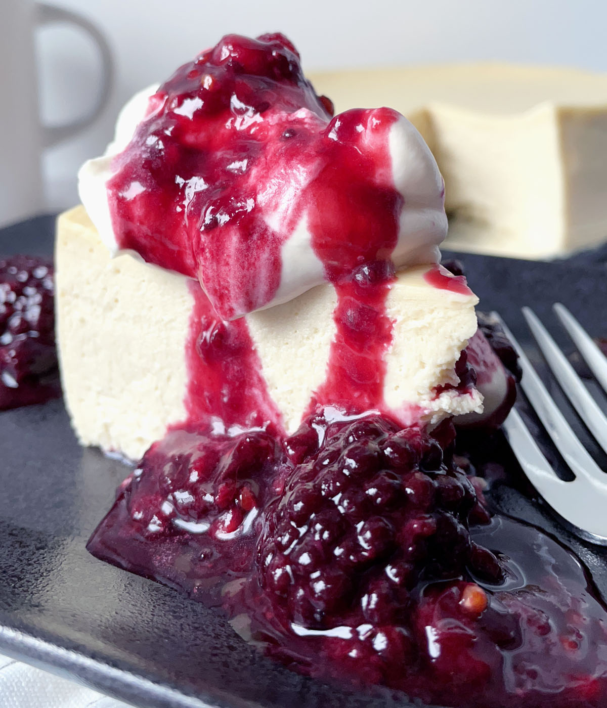 A piece of cheesecake topped with white whipped cream and red berry sauce.