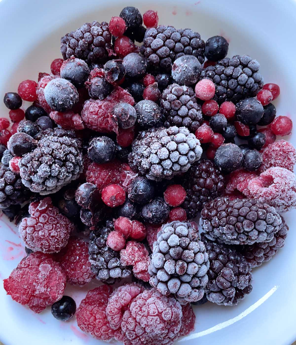 A white bowl containing frozen red and blue and purple berries.