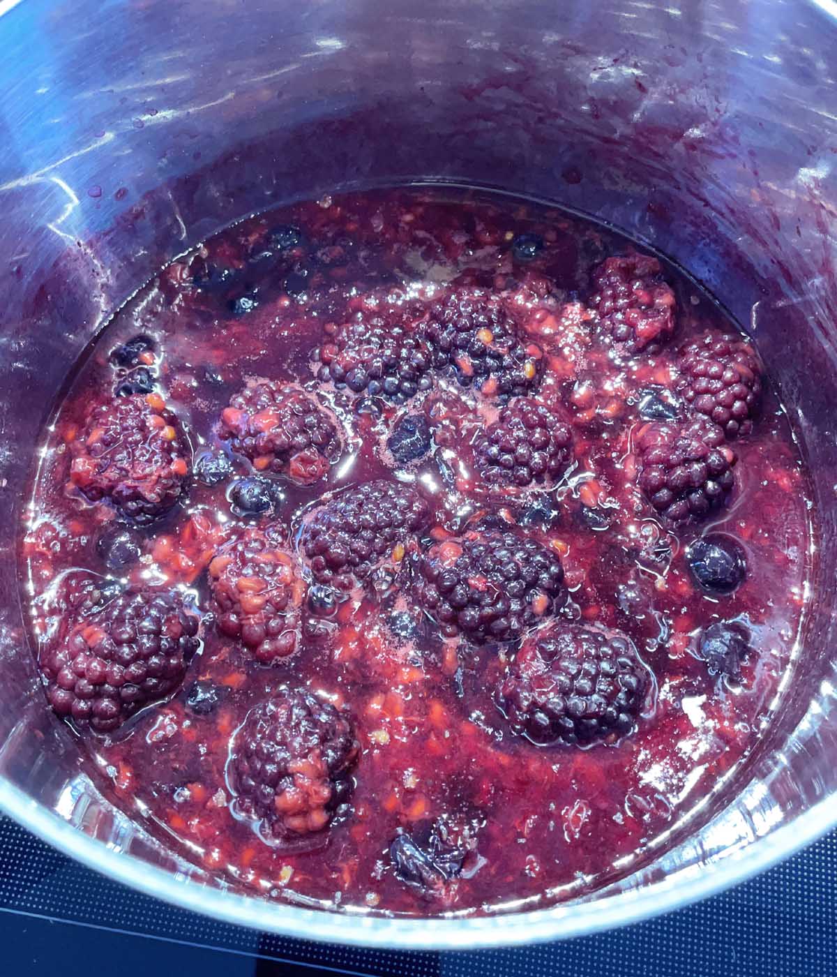 Berries and red liquid cooking in a metal pot.