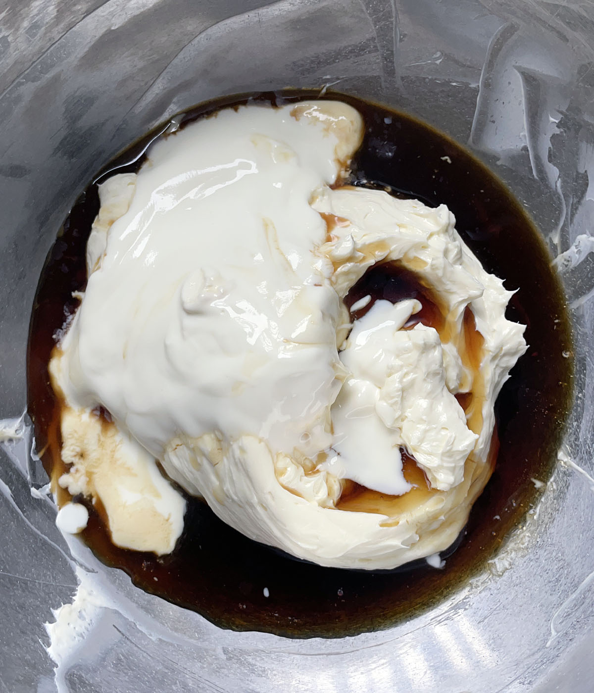 A metal bowl containing beaten white cream cheese, white yogurt, and brown liquid.