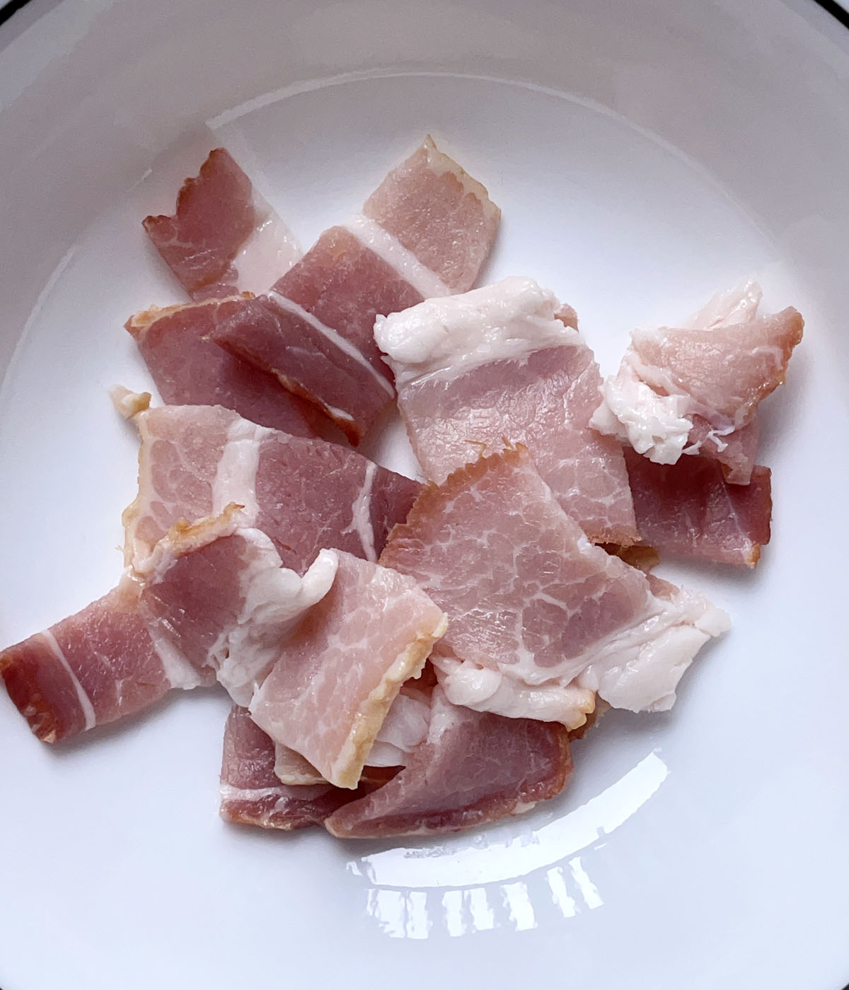 Cut up raw bacon in a white dish.