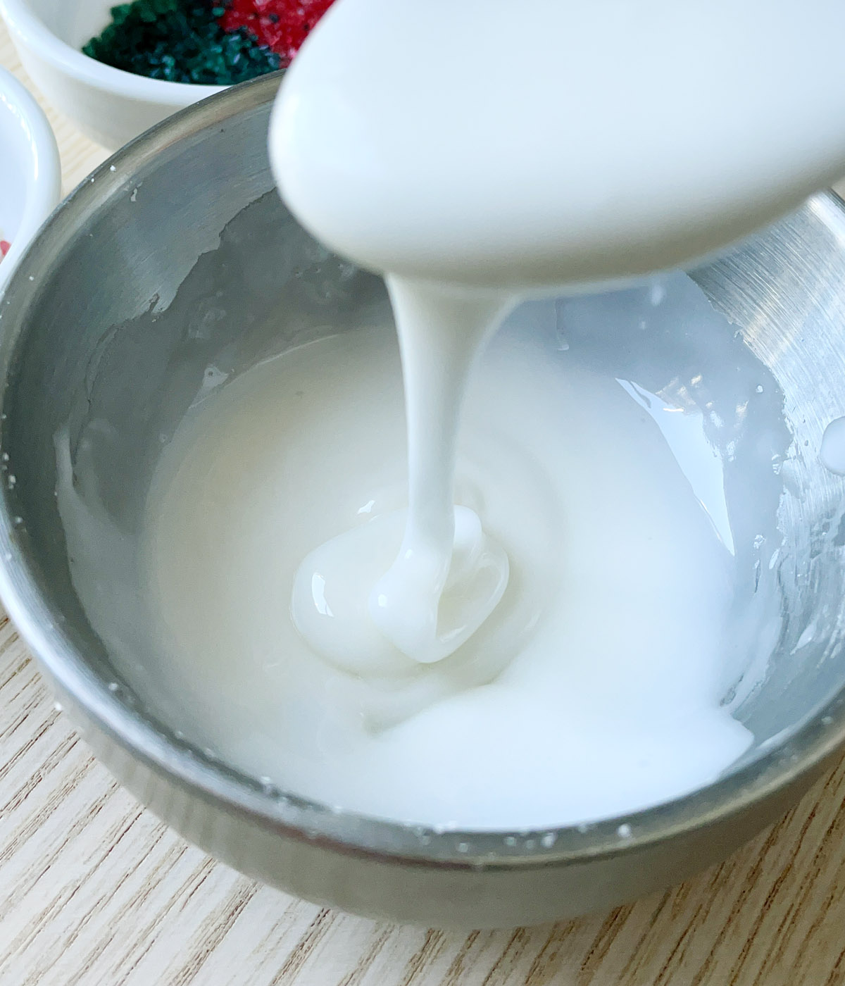 A thick white glaze being drizzled from a spoon into a round bowl.