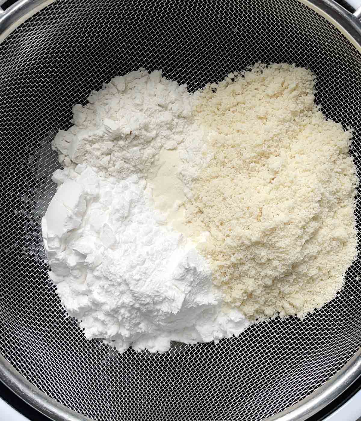 White and yellow dry flour ingredients in a mesh strainer.