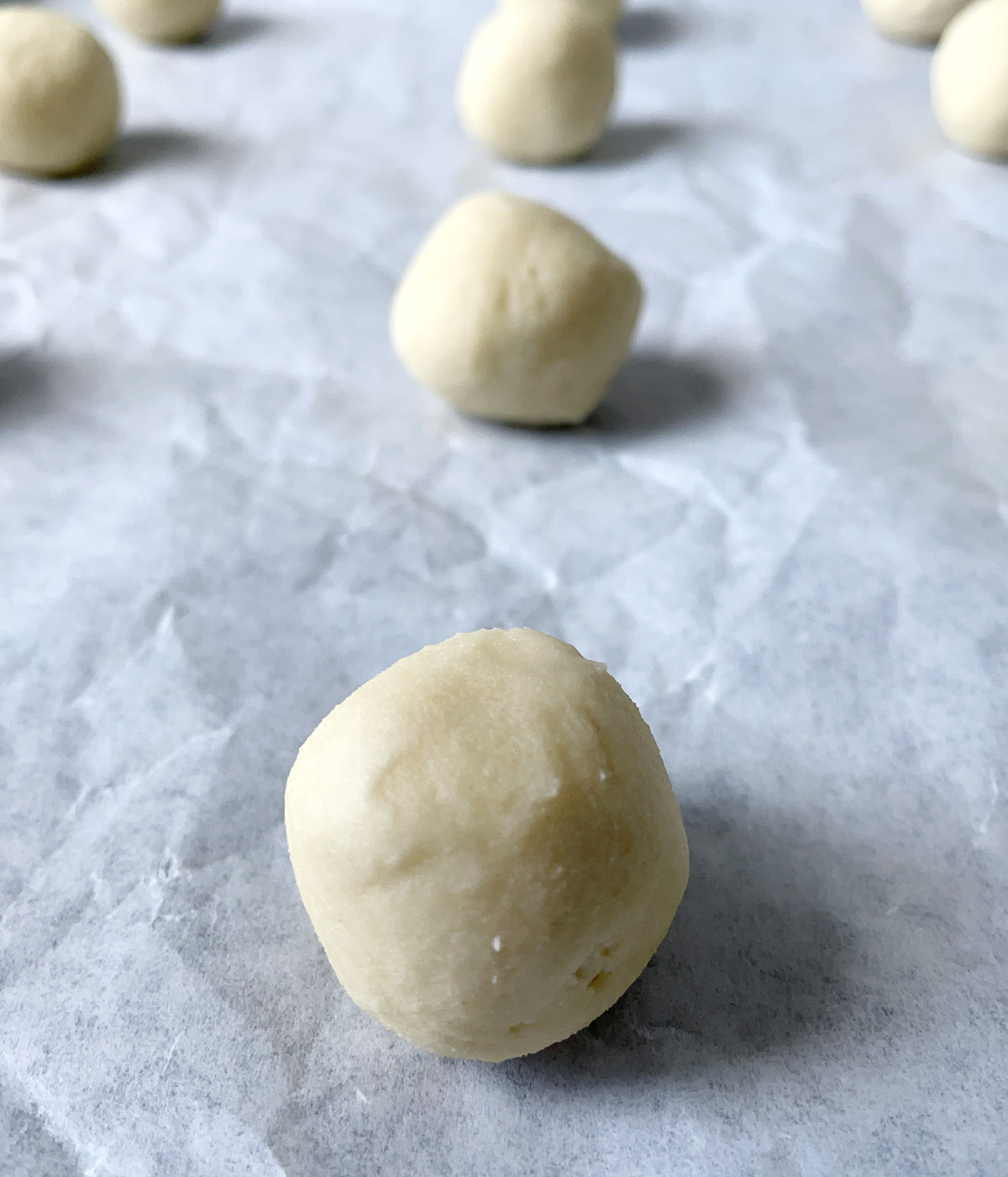 Light yellow round dough balls on a white paper on a baking sheet.