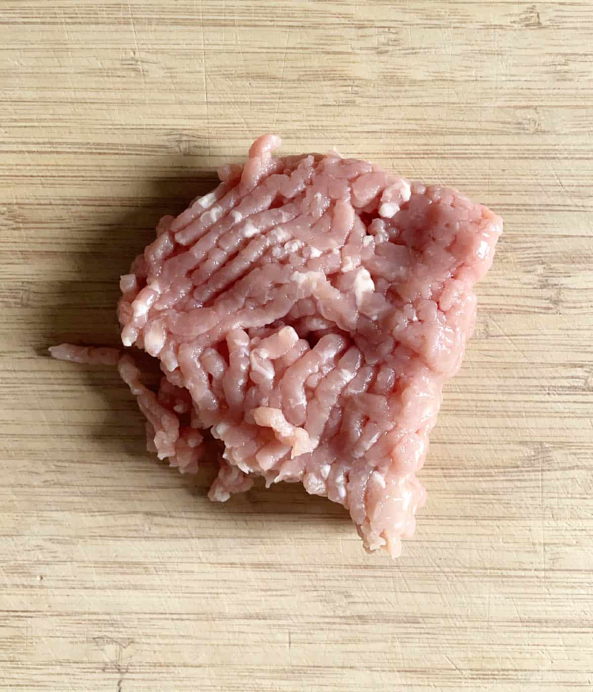 Raw pink ground pork meat on a wooden cutting board.