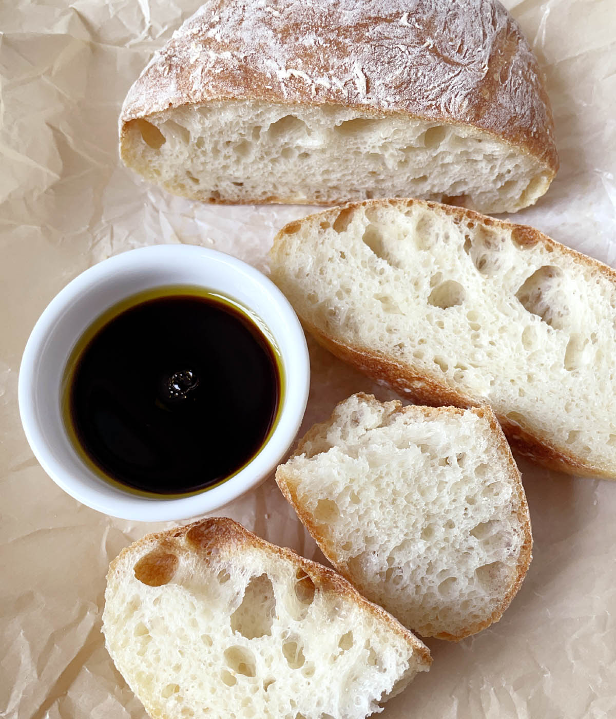 Slices of baked bread next to a white bowl containing oil and black vinegar.