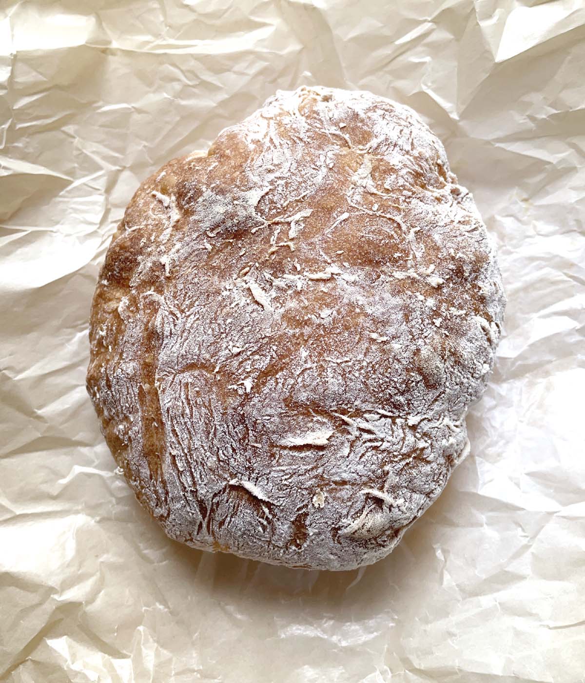 A round baked loaf of ciabatta bread on crumpled piece of baking paper.