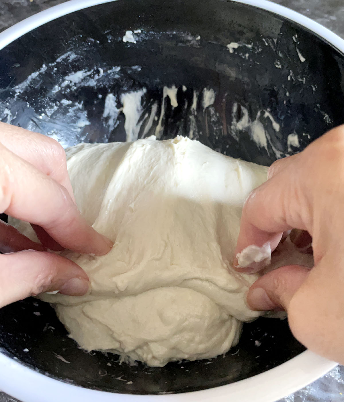 Two hands folding dough over onto itself in a black bowl.