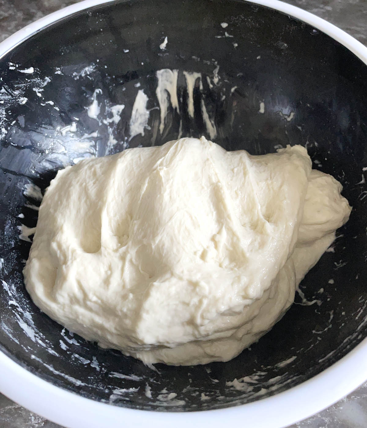 White bread dough in a round black and white bowl.