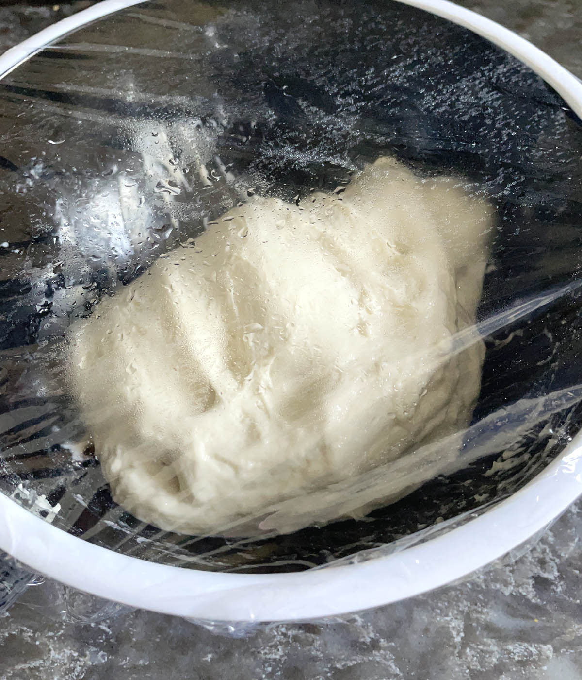 Clear plastic wrap covering a bowl containing bread dough.
