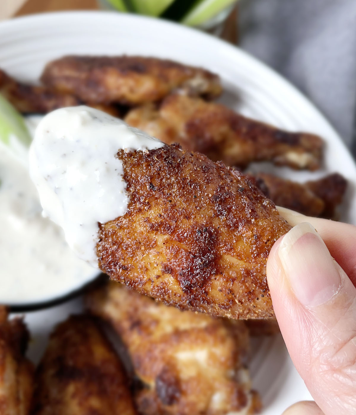Close-up of a hand holding a baked chicken wing with white dip on the tip.