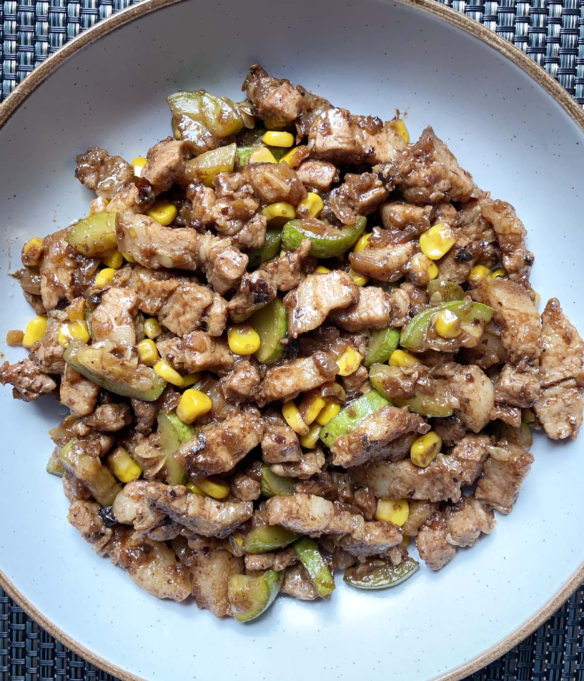 A round dish containing black bean garlic pork belly with zucchini and corn.