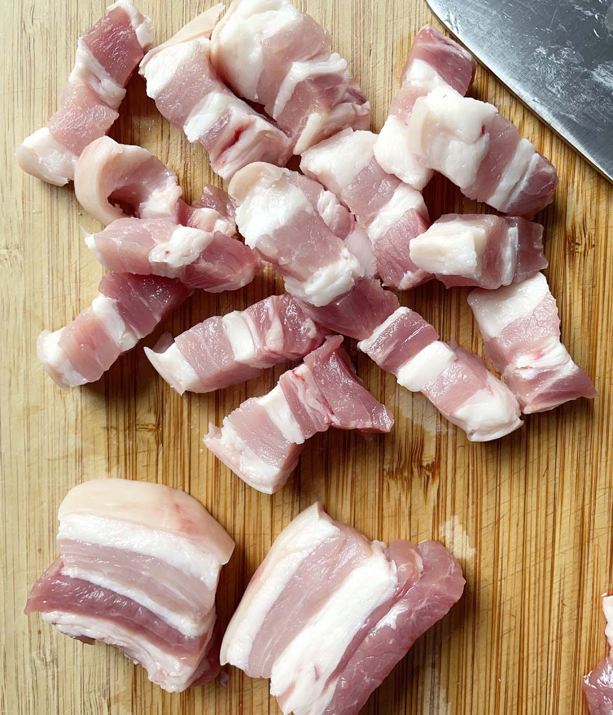 Pork belly that has been cut into small pieces on a wooden cutting board.