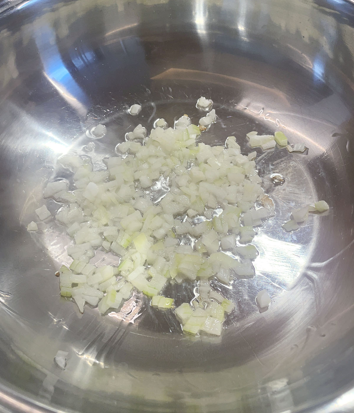 Diced onions frying in a metal pan.