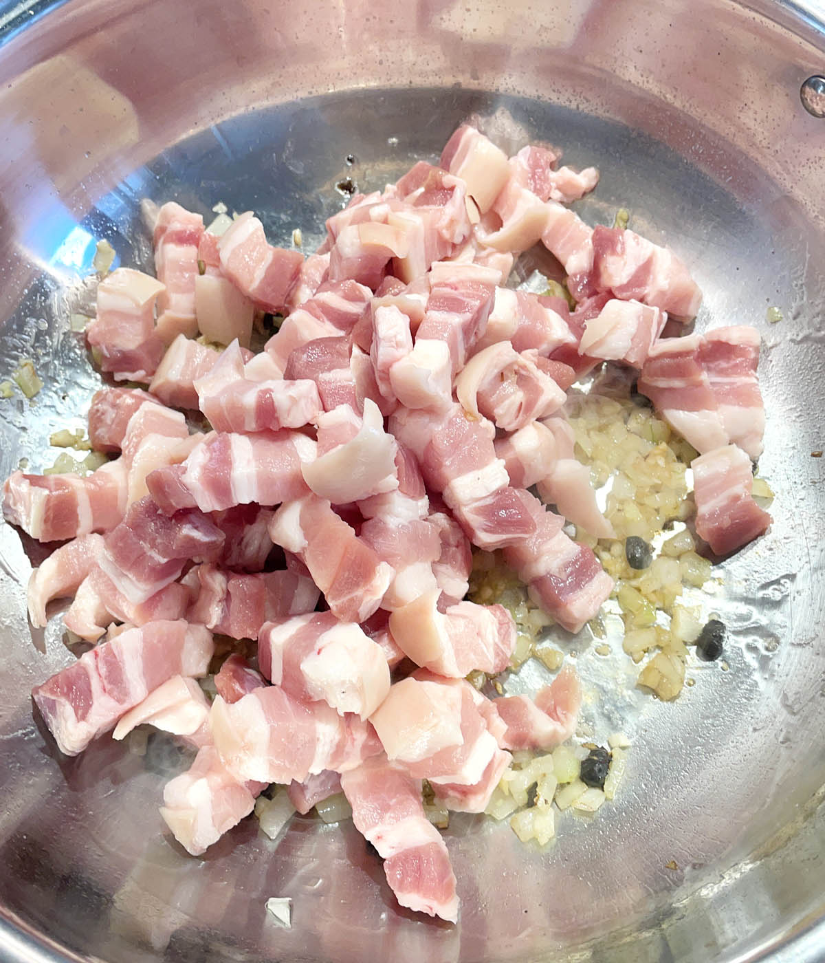 Raw pink pork belly chunks frying in a metal pan.