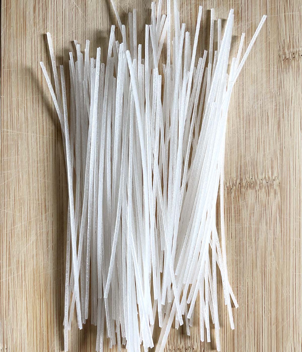 Dry white noodle sticks for making sunomono noodle salad on a wooden cutting board.