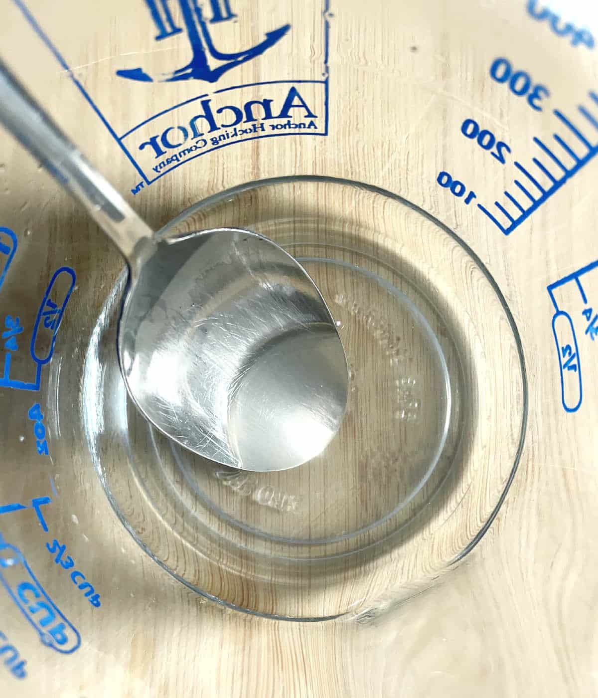 A glass measuring cup containing a clear liquid and a spoon.