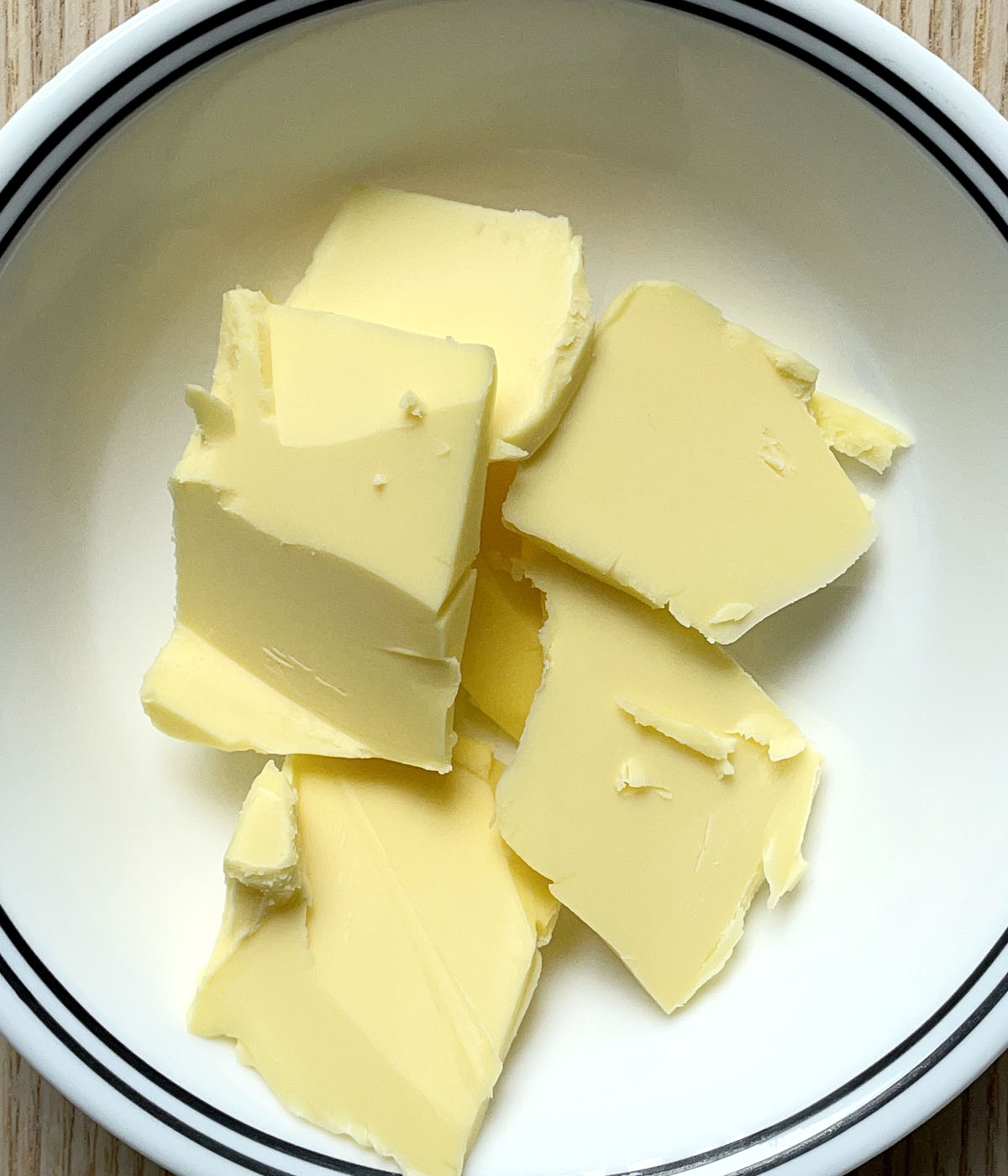 A white round bowl containing chunks of yellow butter.