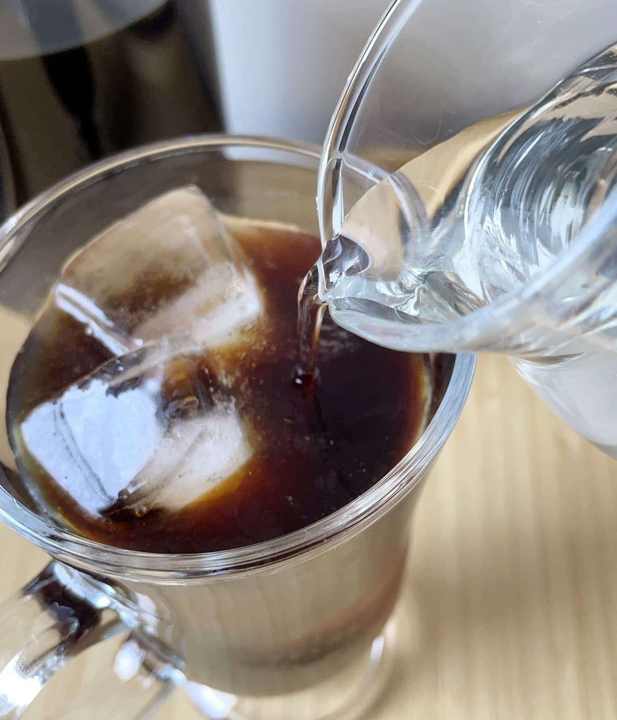Clear simple syrup being poured into a glass of iced coffee.