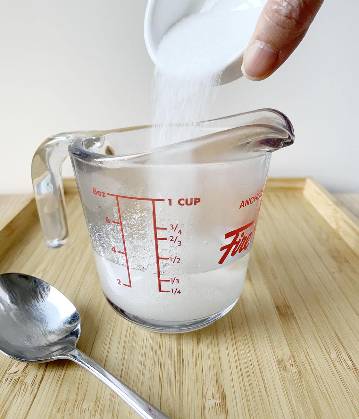 White sugar being poured into a glass measuring cup containing water.