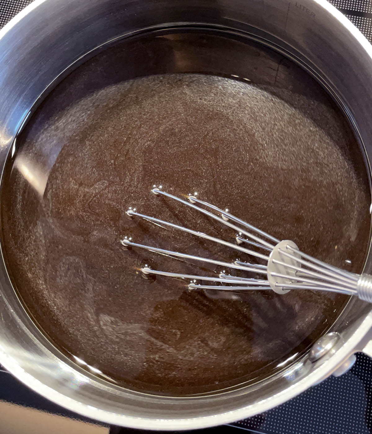 A metal whisk in a metal pot with brown liquid.