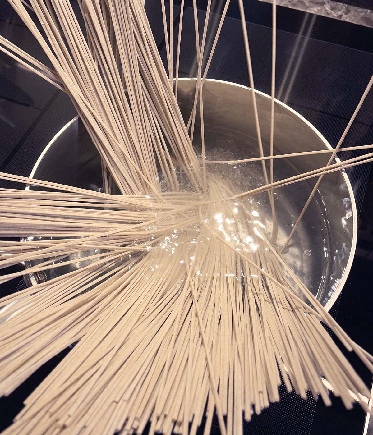 A metal pot with dry noodle sticks in water.