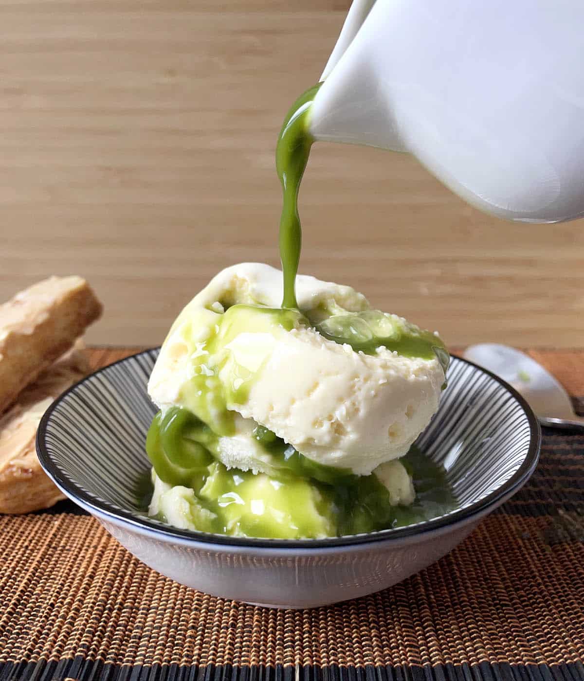 Green matcha tea being poured over two scoops of vanilla ice cream in a black and white dish.