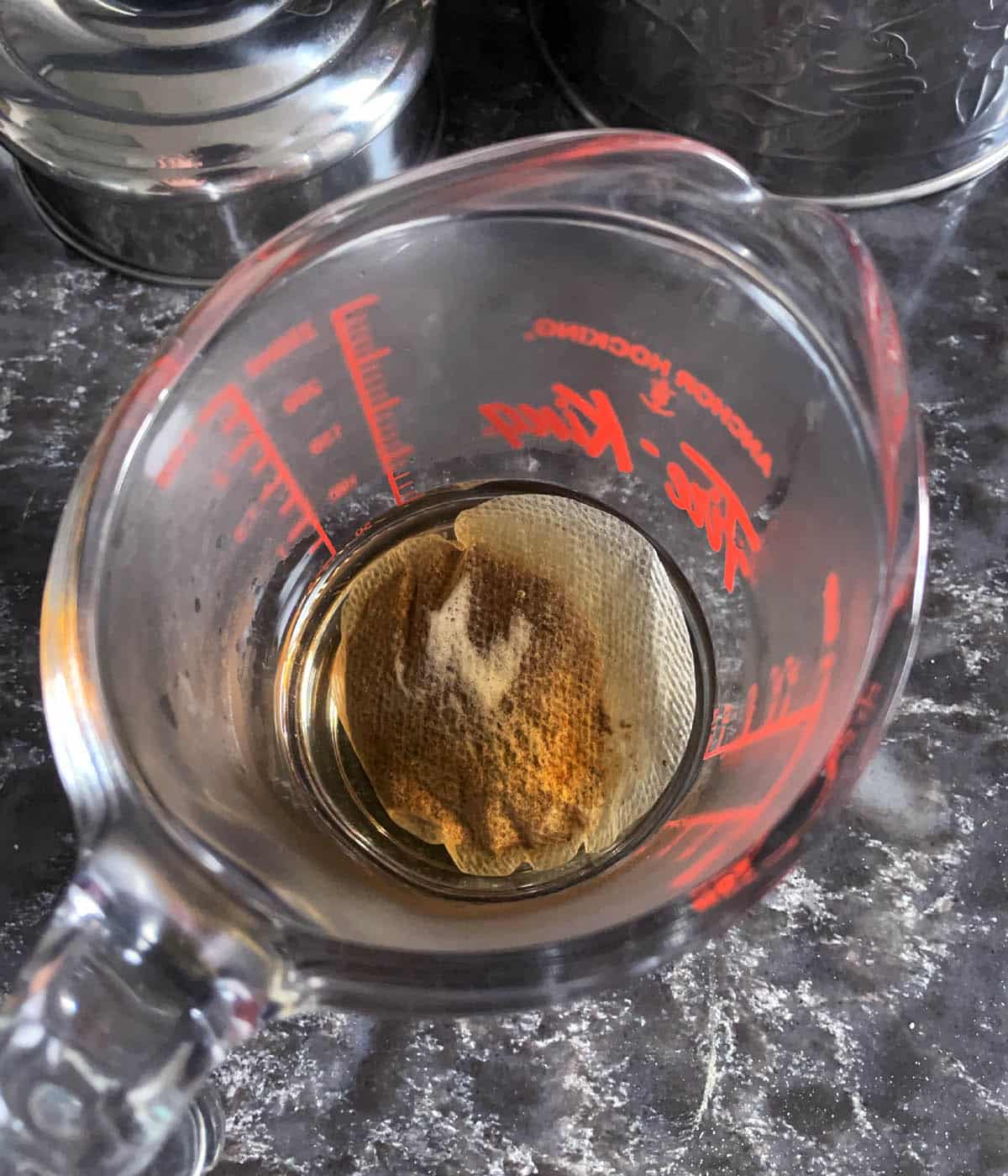 A round tea bag in a glass measuring cup with water.