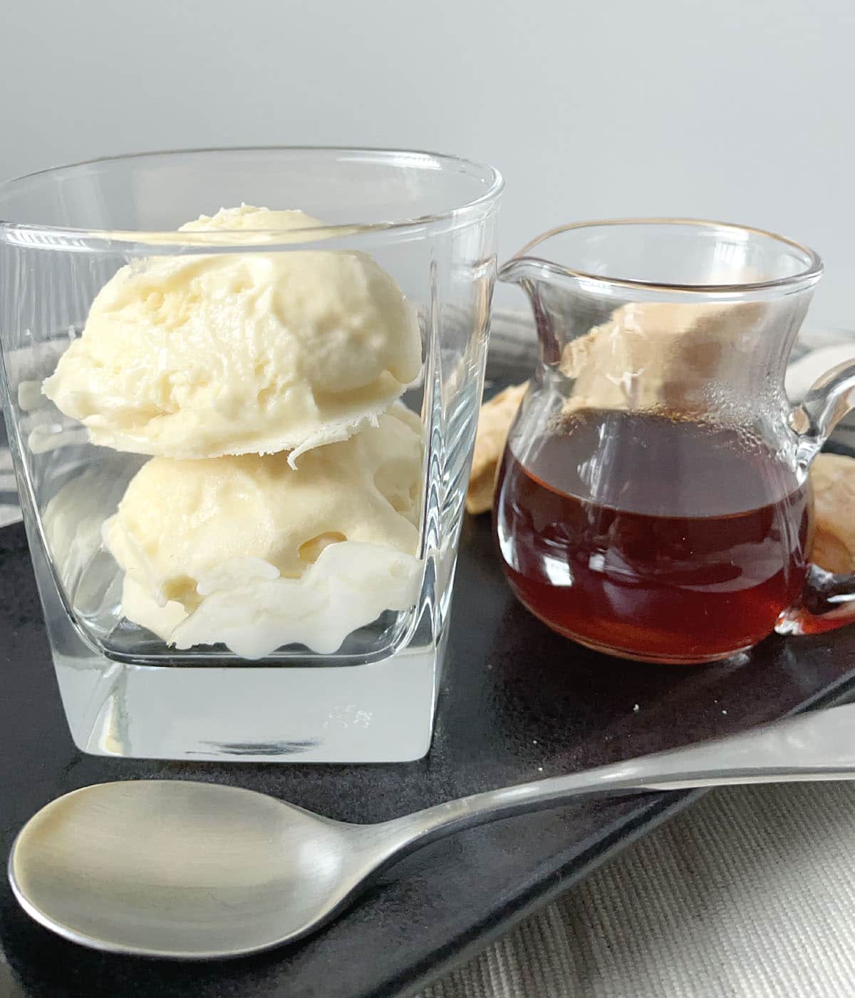 A square glass with two scoops of vanilla ice cream, a small glass pitcher containing brown tea.