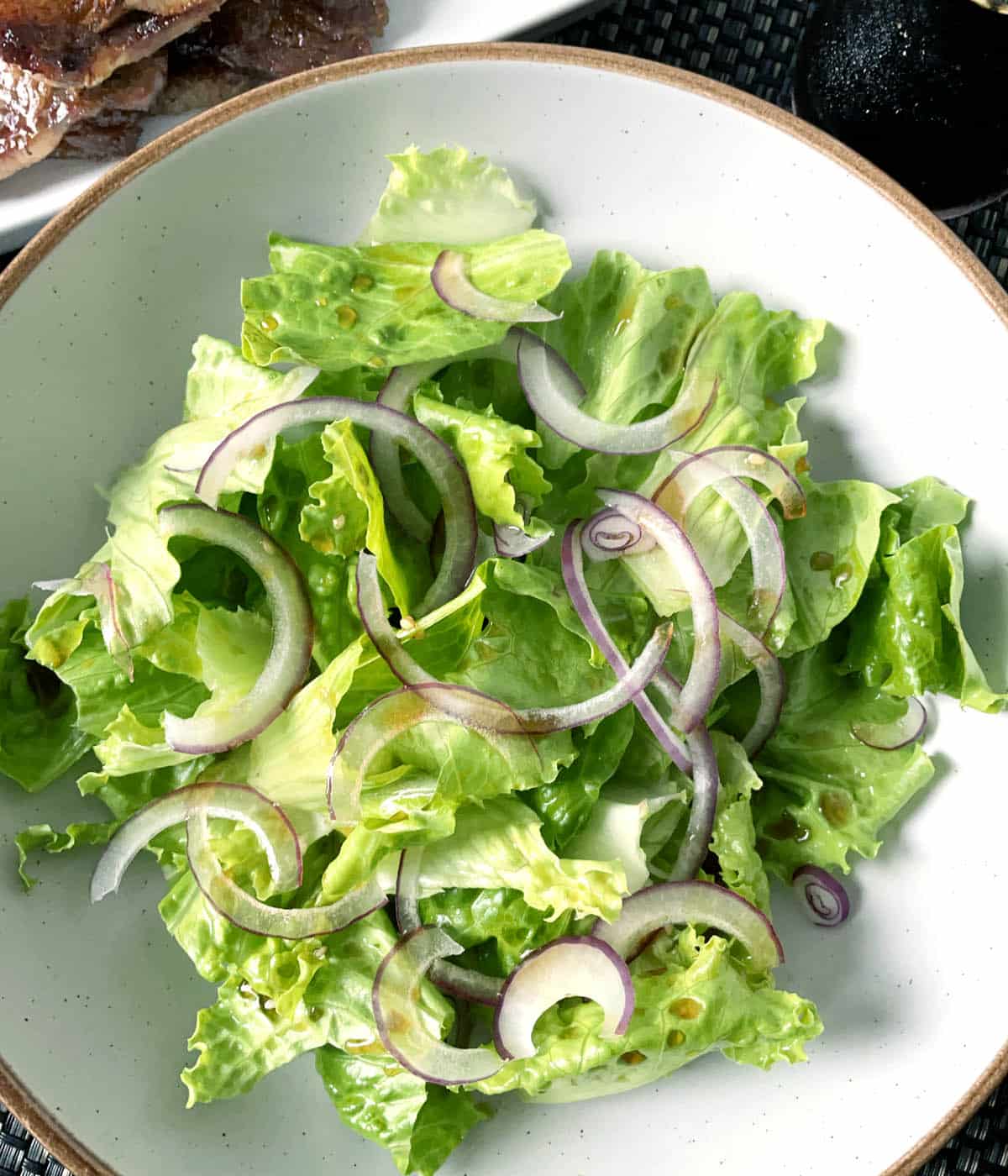 A round dish containing Korean lettuce salad with thinly sliced red onions and brown dressing.