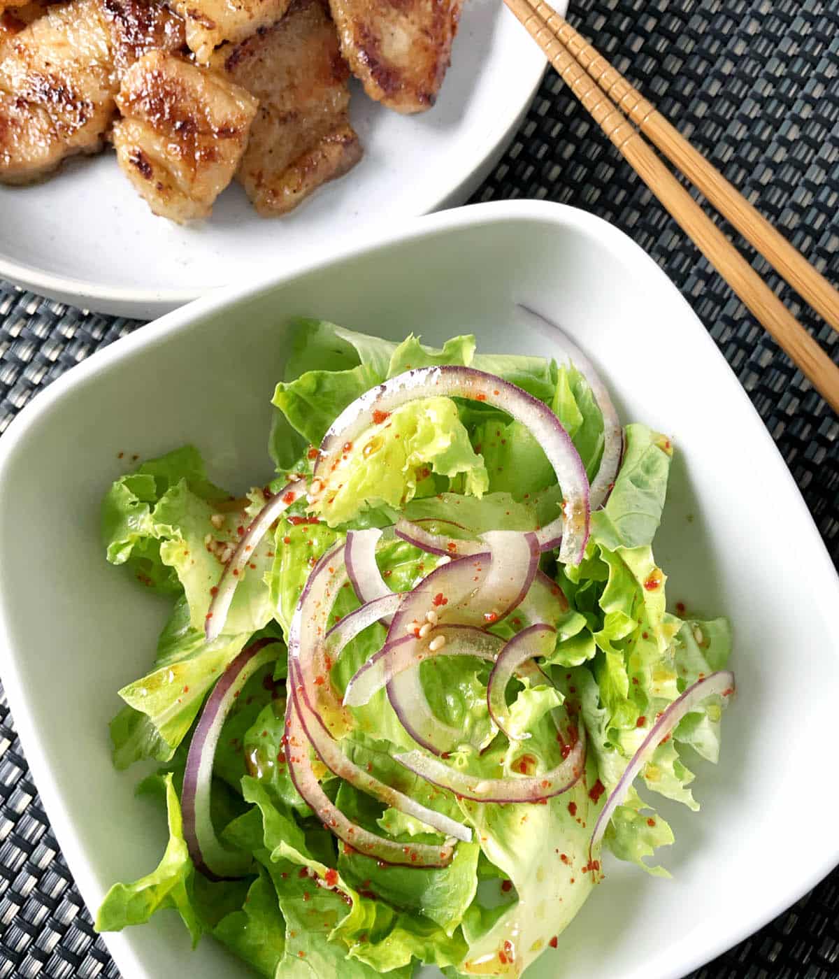 A square white dish containing Korean lettuce salad with thinly sliced red onions and red pepper flakes.