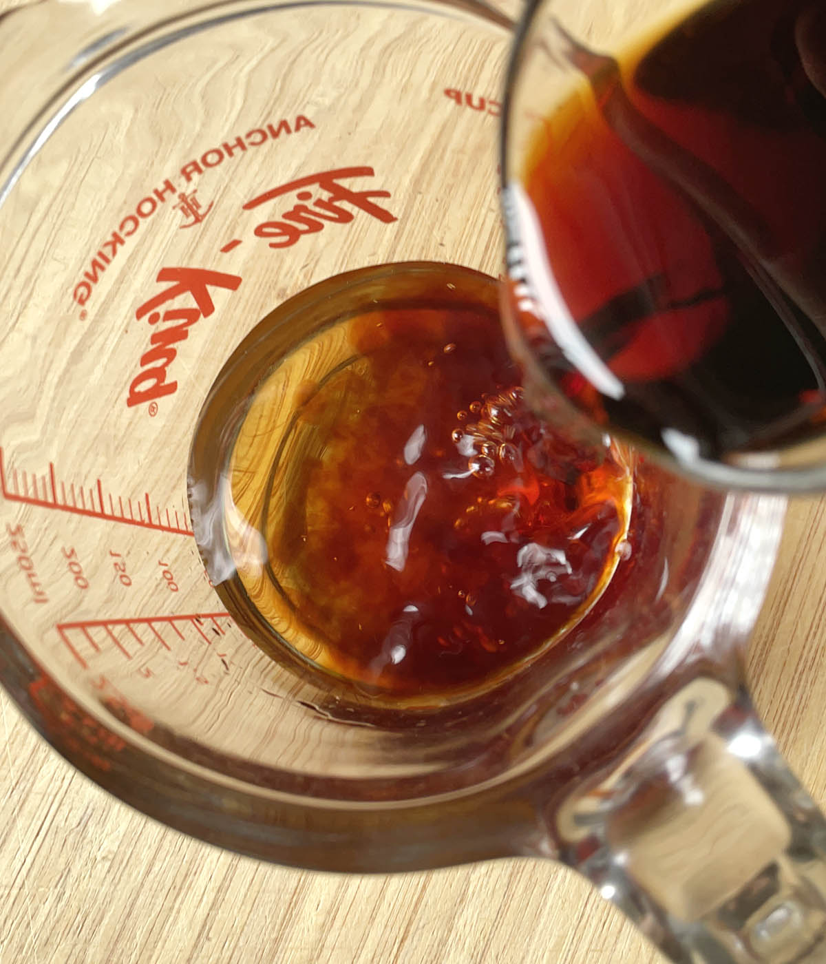 Brown soy sauce being poured into a glass measuring cup.