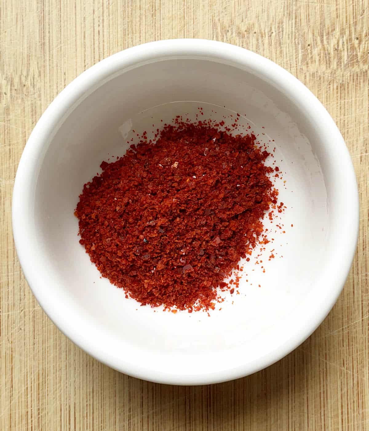 A round white dish containing red chili pepper flakes.