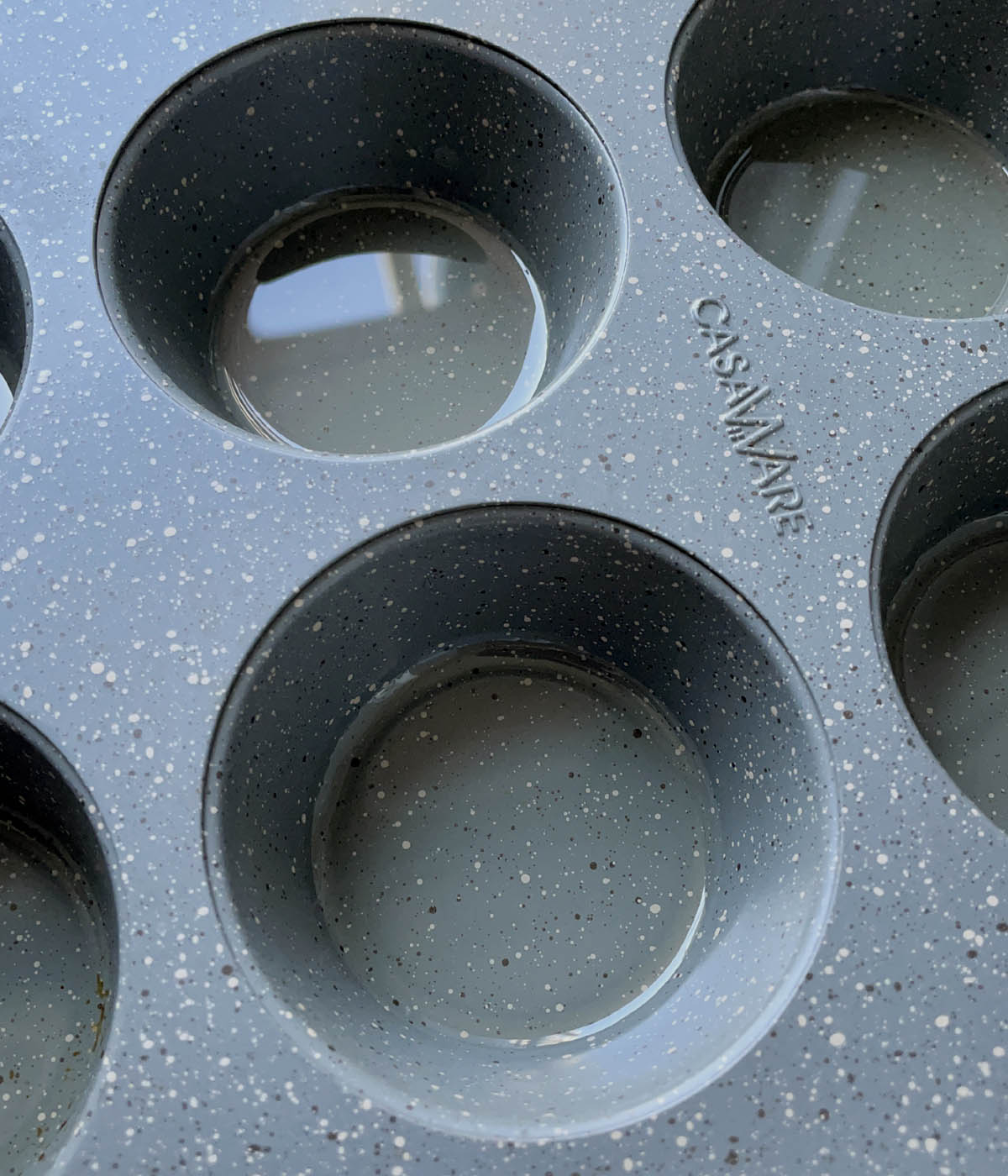 A grey speckled metal muffin tin with some oil in the cups.