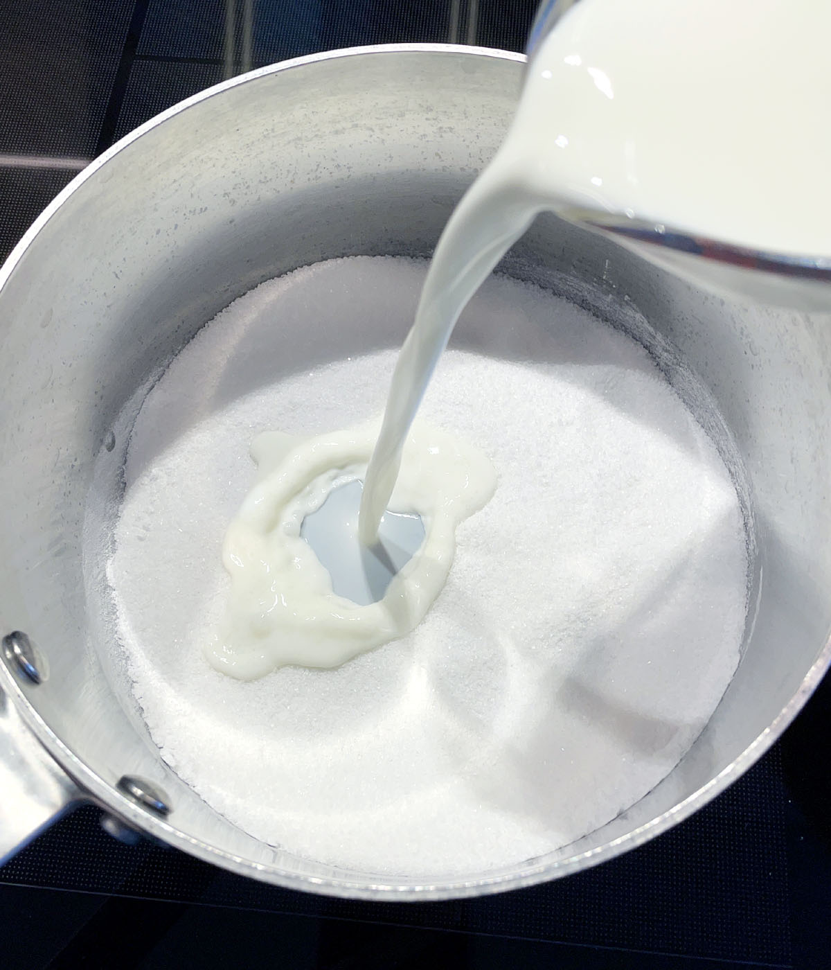 Milk being poured into a pot containing white sugar and powder.