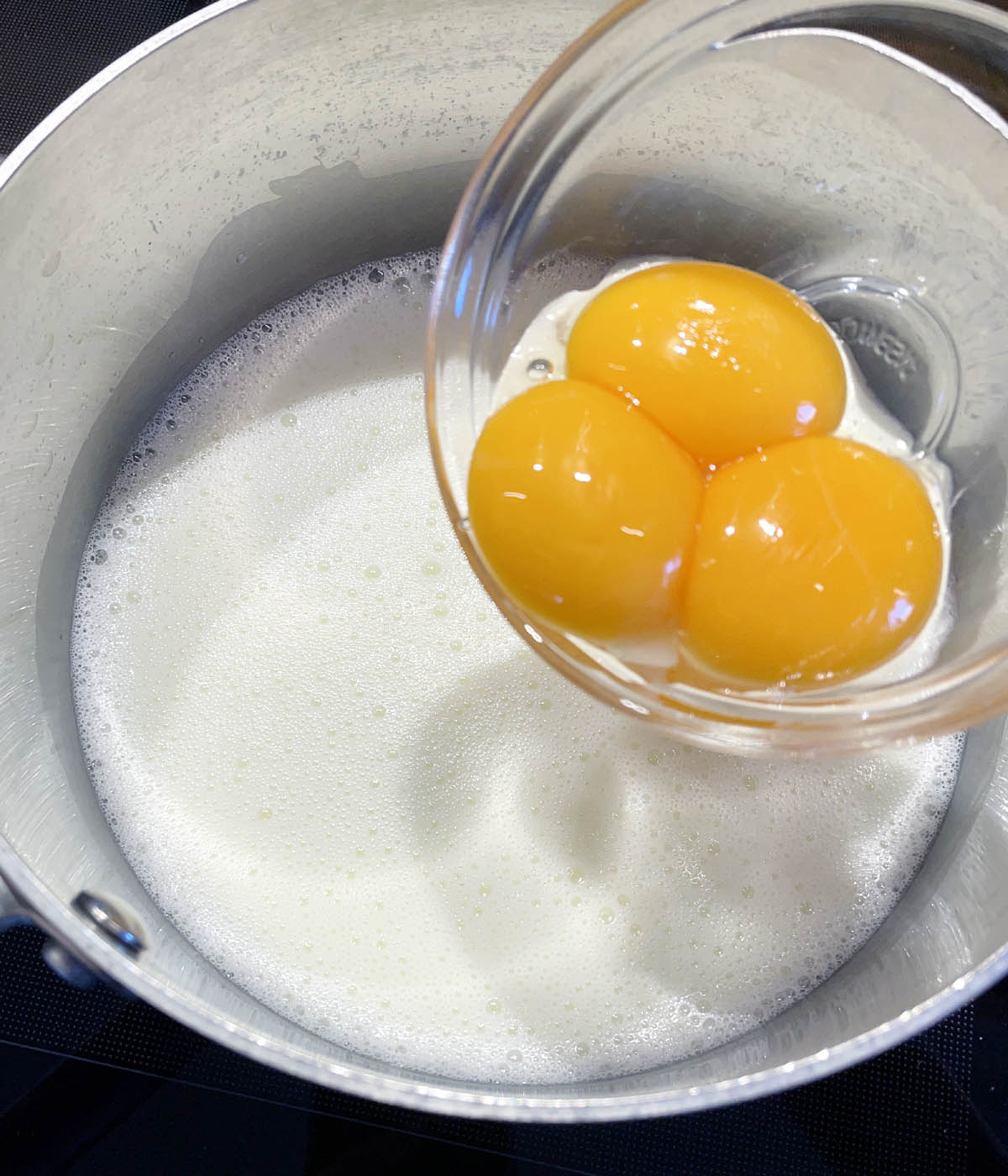 Three egg yolks over a pot of white liquid.